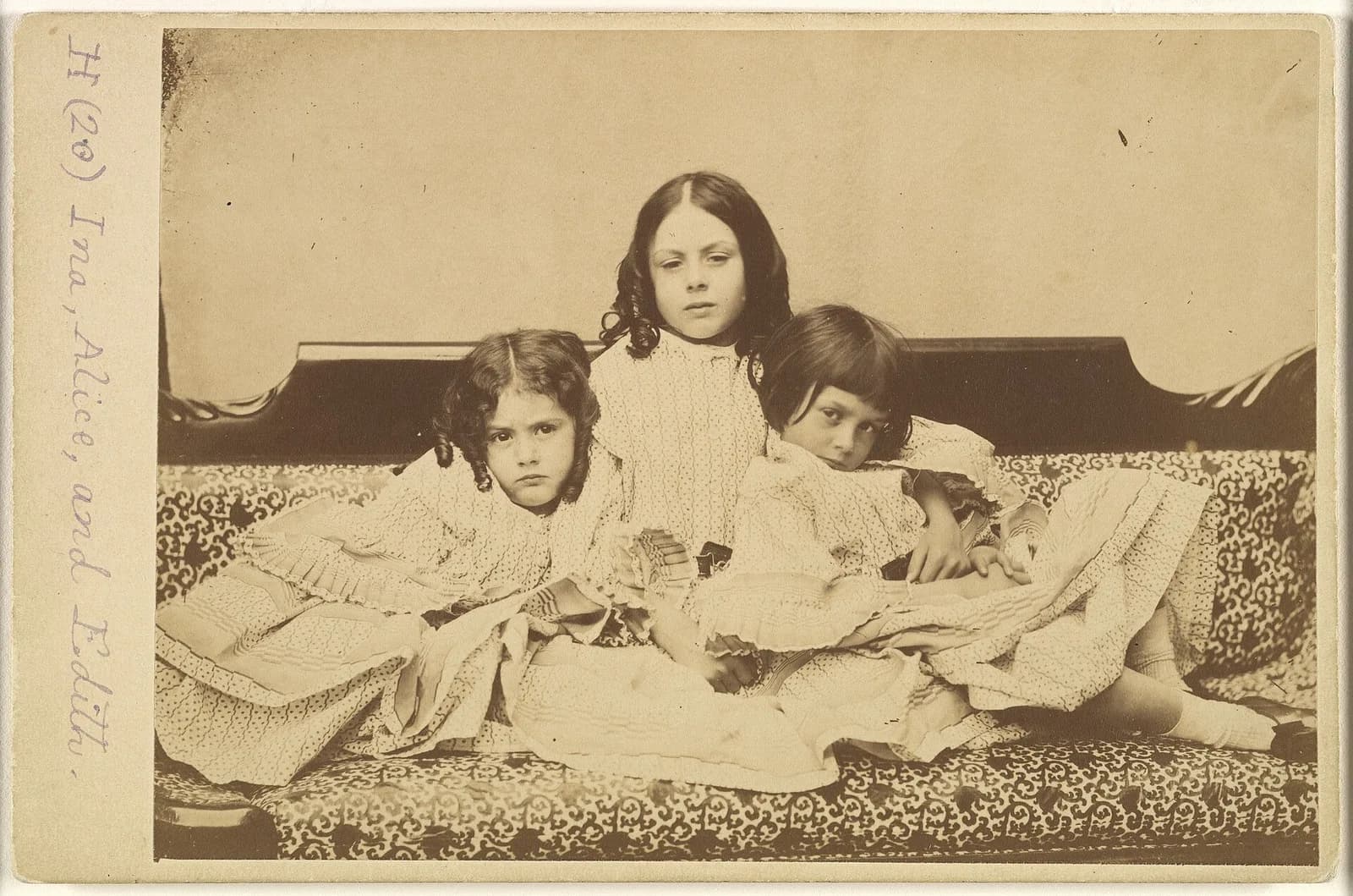 Lewis Carroll's 1858 photograph of the three Liddell sisters, Ina, Alice and Edith, lying together on a patterned sofa in pale summer dresses, Alice resting her head on her arm at the right