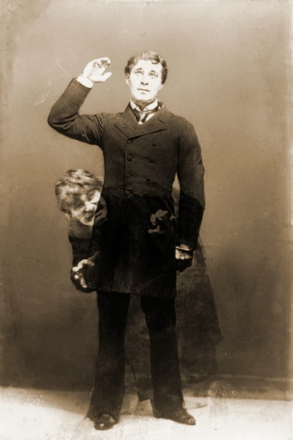 A sepia double-exposure stage photograph of Richard Mansfield as Dr Jekyll, standing upright in a dark frock coat with one hand raised, while a crouching, leering Mr Hyde peers out from behind his coat tails