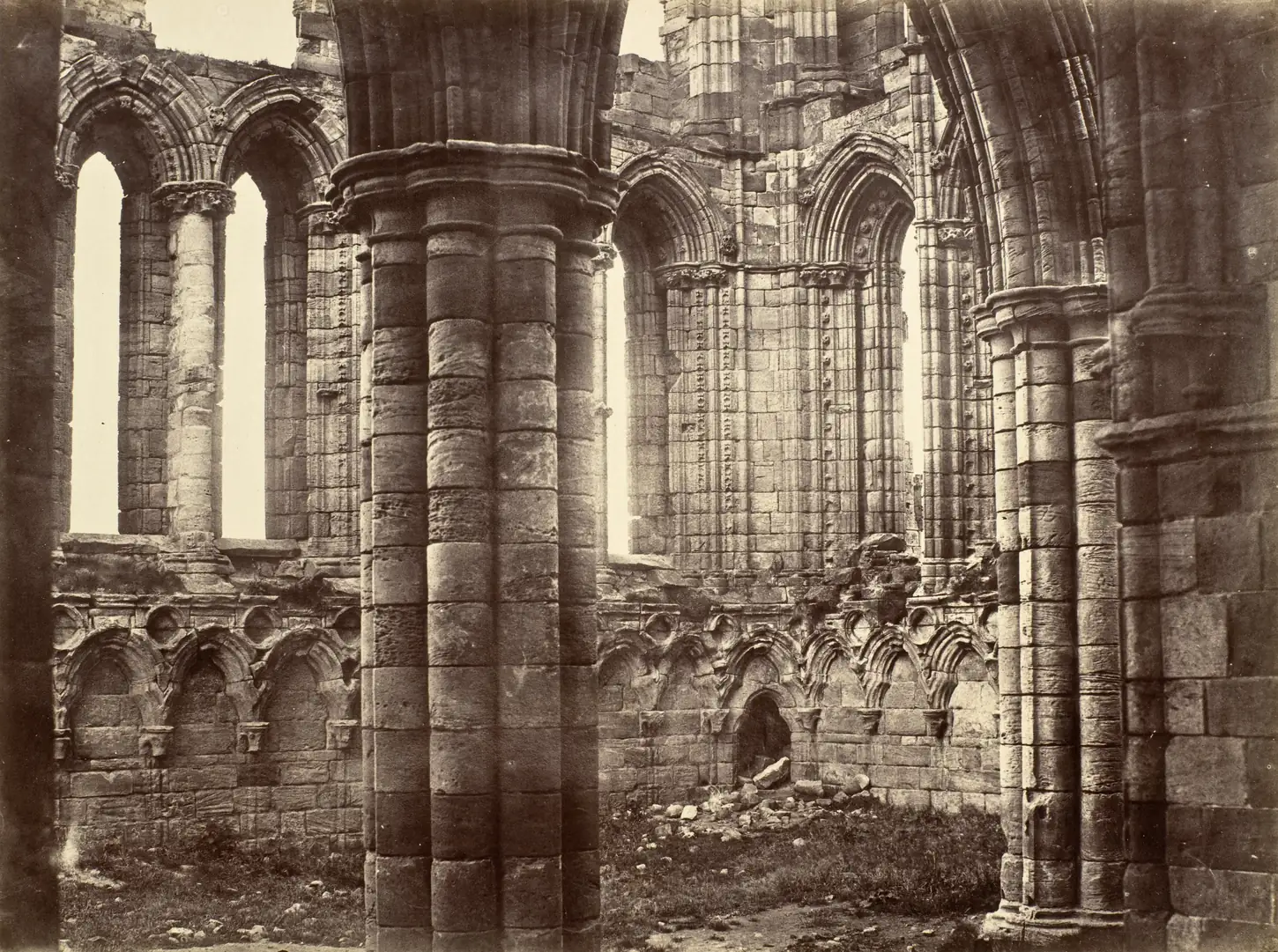 A sepia albumen photograph from about 1854 of the roofless ruined Gothic arches and columns of the north transept of Whitby Abbey in Yorkshire
