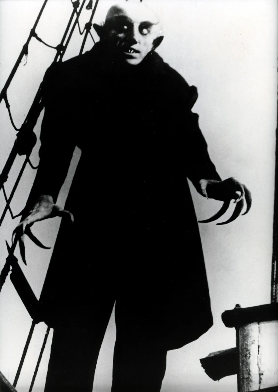 A still from the 1922 silent film Nosferatu showing Max Schreck as Count Orlok, in makeup and claws, standing among the rigging on the deck of a sailing ship