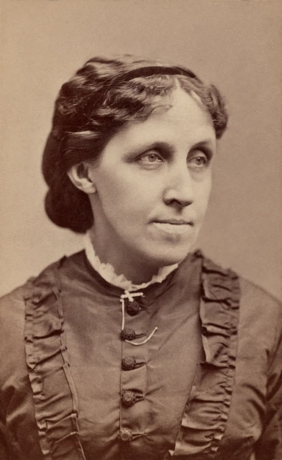 A sepia carte-de-visite photograph of Louisa May Alcott around 1870, in a dark ruffled dress with a white collar, looking slightly away from the camera