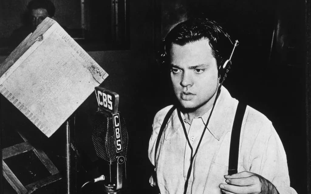 Orson Welles in shirtsleeves at a CBS radio microphone in 1938, headphones on, reading from a script stand