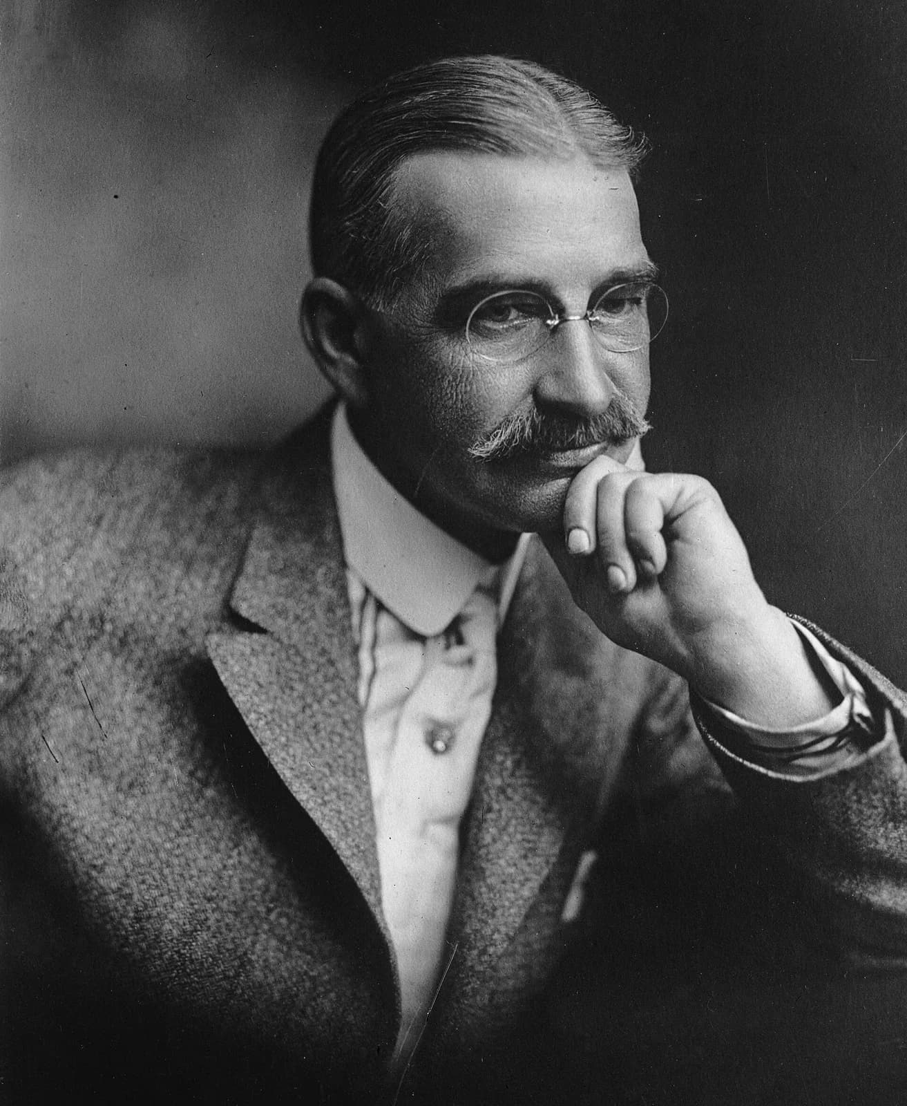 A black-and-white studio portrait of L. Frank Baum around 1911, a moustached man in a dark suit and tie looking slightly to one side