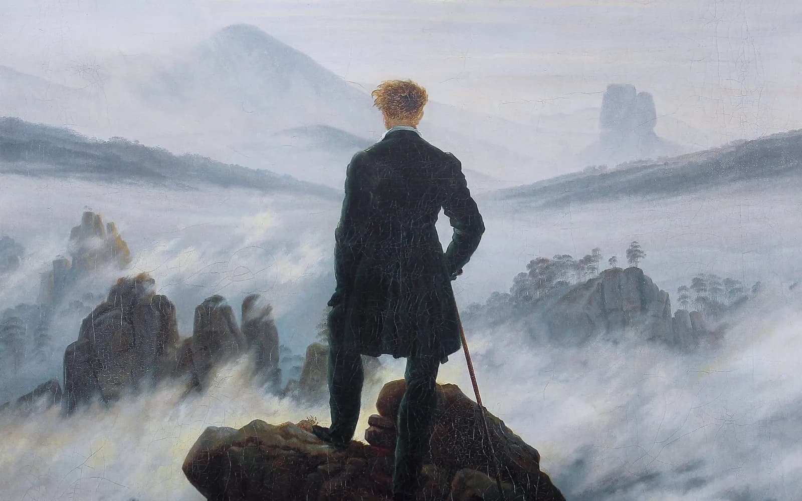 Caspar David Friedrich's painting of a man in a dark coat standing with his back to the viewer on a jagged rock outcrop, one hand on a cane, looking out over a valley of drifting fog toward distant peaks